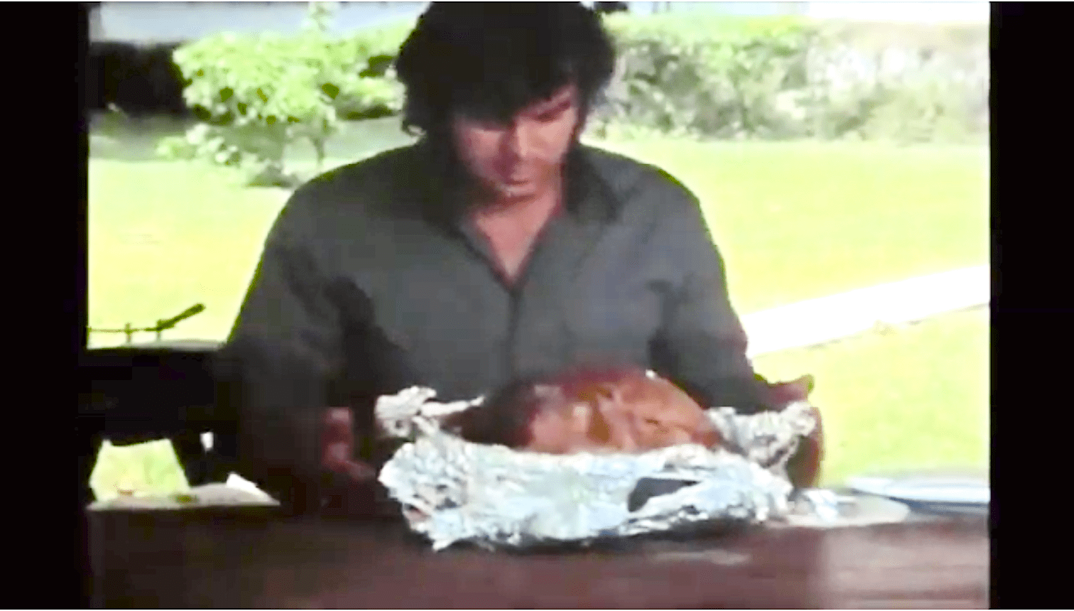 Scene from Blood Freak: a seated man stares at a whole cooked turkey in foil