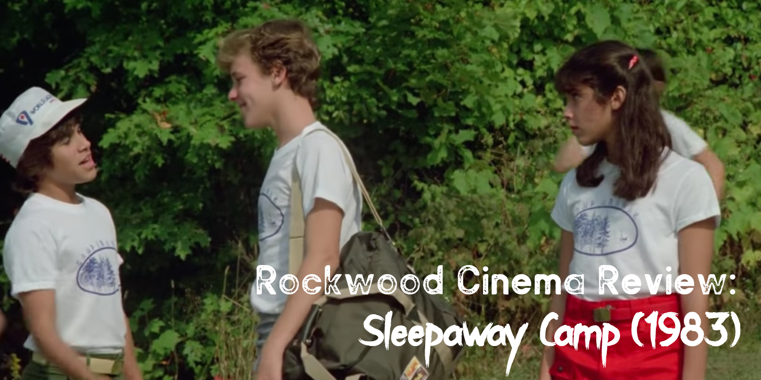 Two guys talk while a girl looks on. They are all wearing the same camp shirt and are in the forest.