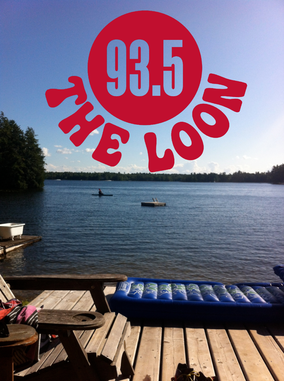 Dock near the lake with chairs and floating mattress with trees in the distance. The 93.5 Loon logo in the horizon.