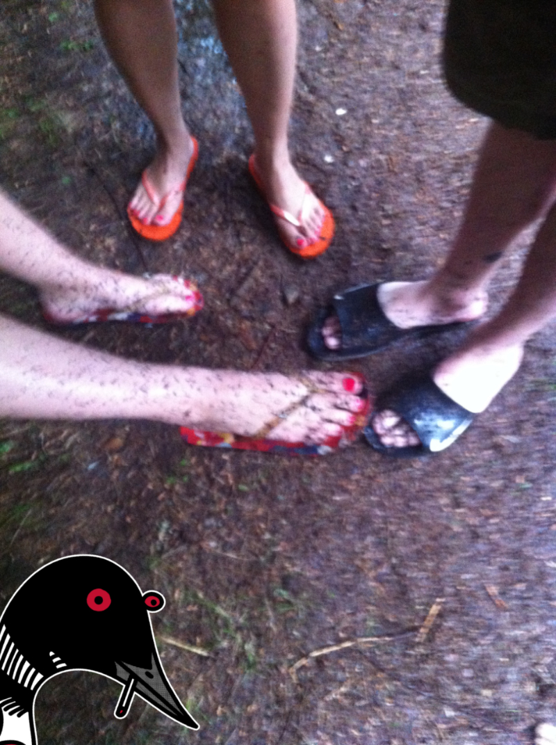 Three pairs of legs and feet in sandals covered in mud