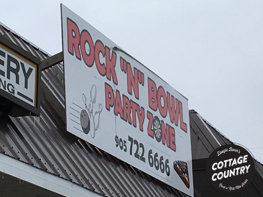 A sign that says Rock N Bowl Party Zone and has bowling ball striking down pins and triangularly racked billiard balls