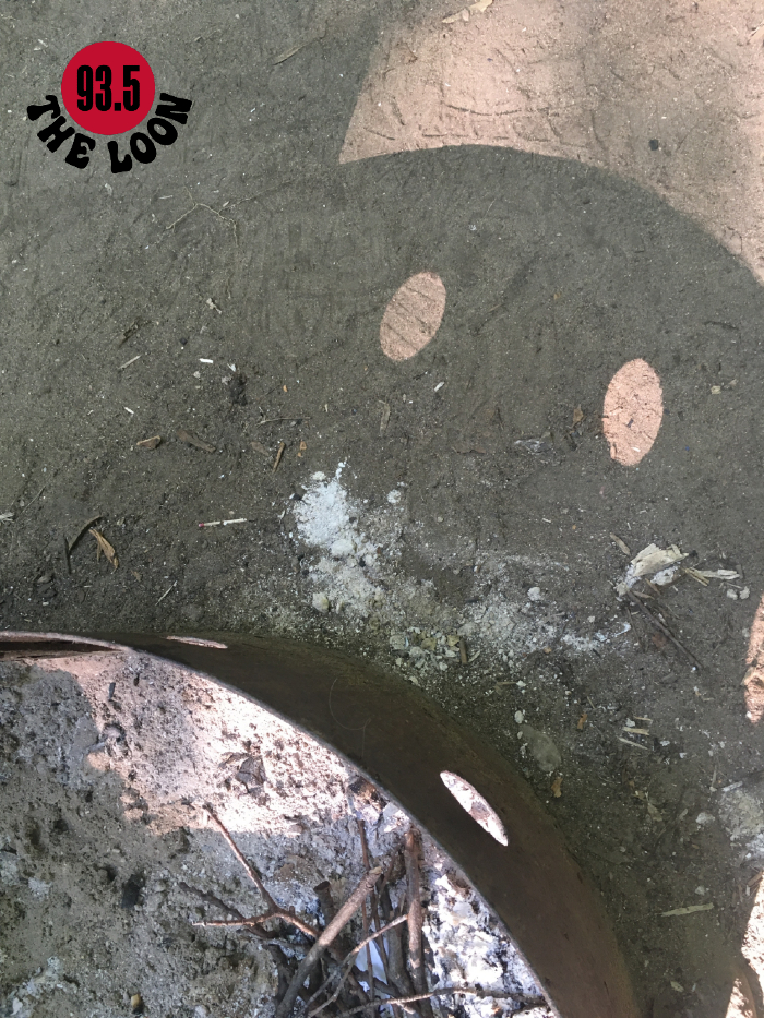 The shadow from a provincial park BBQ grill look like a face and eyes, with ashes strewn on the ground that look like a smile