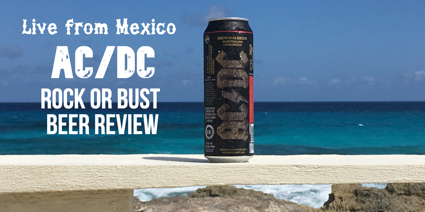 A black tall can of beer with the AC/DC logo scrolled on its side stands on a concrete ledge near the ocean
