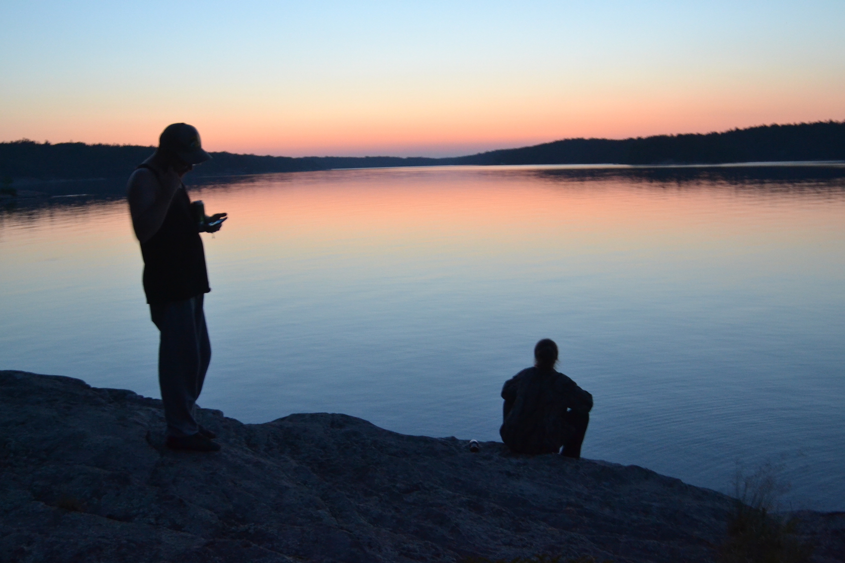 Silhouettes stand dubiously against a lake during sunset